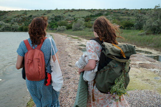 Two women walking along the shoreline with backpacks