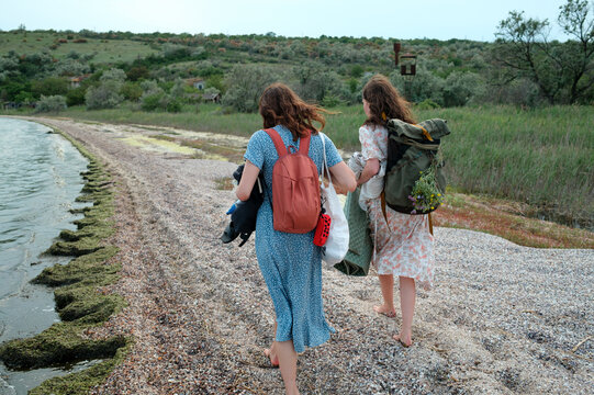 Two women walking along the shoreline with backpacks