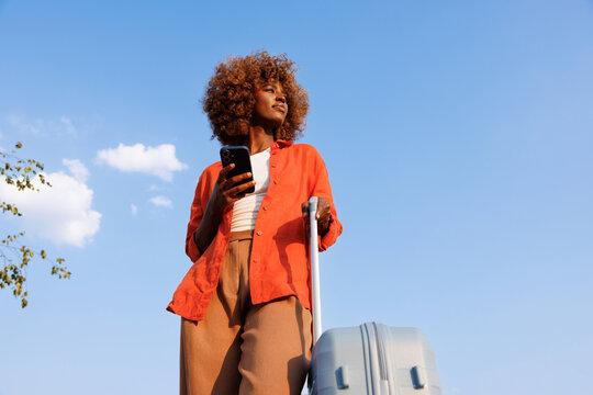 Woman with smartphone and suitcase under summer sky