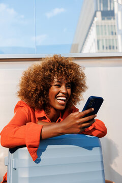 Woman using smartphone while leaning on blue suitcase