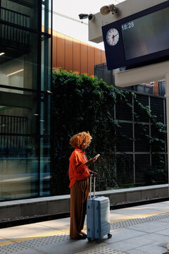 Woman checking smartphone beside suitcase on platform