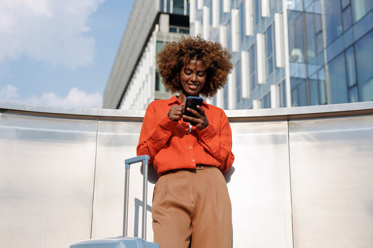 Business woman using smartphone beside suitcase office building