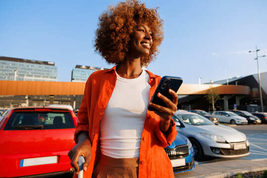 Woman checking smartphone beside suitcase in parking area