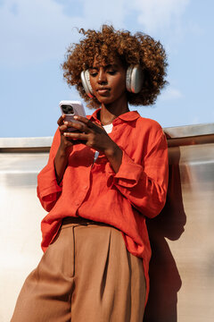 Woman using smartphone with headphone in orange shirt under sky