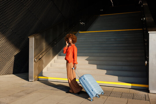 Woman with earphones pulls suitcase beside stairs