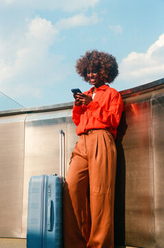Woman using smartphone beside suitcase under blue sky