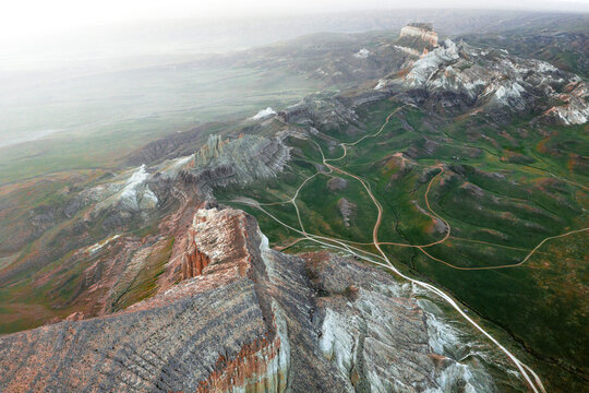 Aerial view of the rugged Airakty rock formations rising above the green grassy plains and winding dirt paths in the vast landscape of Shetpe, Mangystau Region, Kazakhstan.
