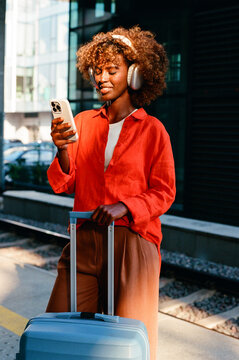 Woman checking smartphone with suitcase on city street