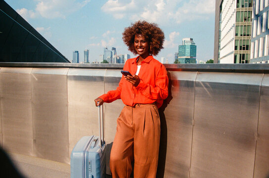Woman portrait checking smartphone beside blue suitcase film photo