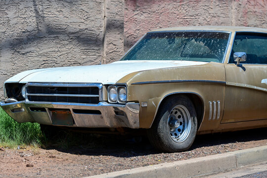 Abandoned old car with faded paint, missing headlight and visible wear parked beside a wall, illustrating vehicle deterioration, neglect, aging, and automotive decay