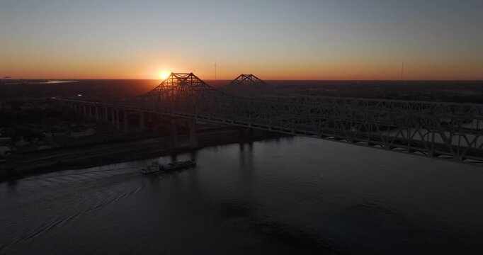 Aerial pull-back as a barge passes beneath first light through a Mississippi River bridge