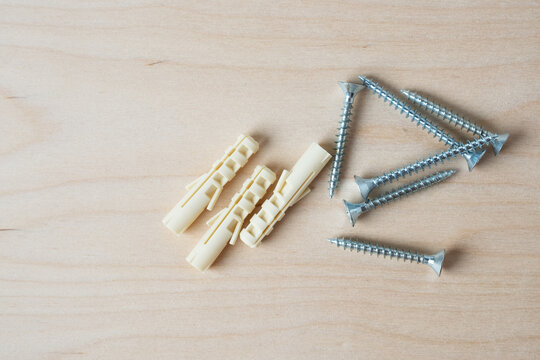 Plastic wall anchors and metal screws on wooden background