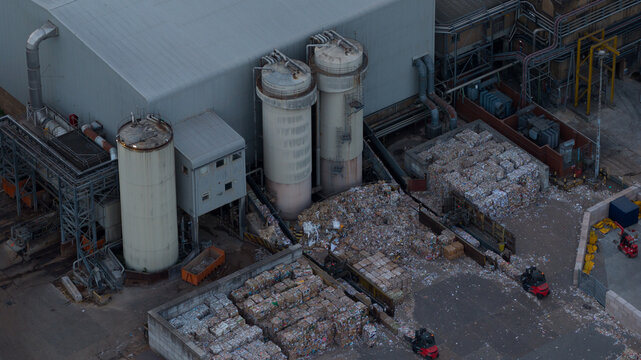 Aerial view of an industrial recycling facility featuring large storage tanks and stacks of baled paper with forklifts operating in the yard in Sittingbourne, England, United Kingdom.