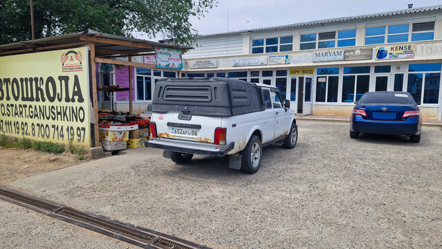 White VIS-2346 pickup based on the Lada Niva, with a hardtop and Kazakh license plate, parked in front of shops in Kurmangasy (Ganyushkino); commercial vehicle, Atyrau, Kazakhstan 14.05.2025
