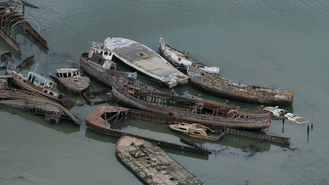 Aerial view of Hoo Sailing Barge Graveyard featuring several abandoned, decaying wooden barges and shipwrecks resting in the shallow tidal waters of the River Medway, Kent, United Kingdom.
