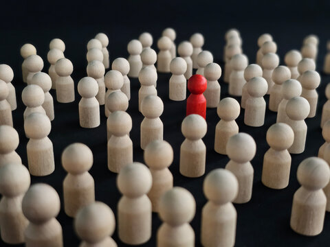 Wooden figures in a crowd with one red figure standing out against
