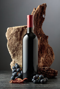 Bottle of red wine with stone, dried snags, and blue grapes.