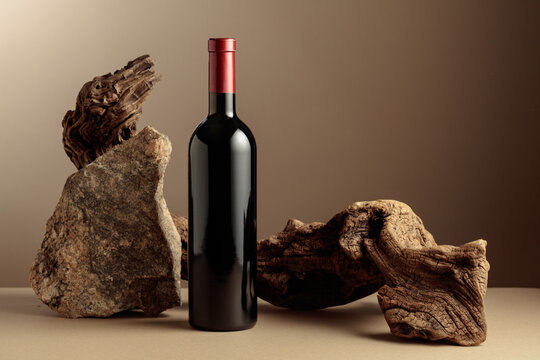 Bottle of red wine with old snag and a piece of granite rock on a beige background.