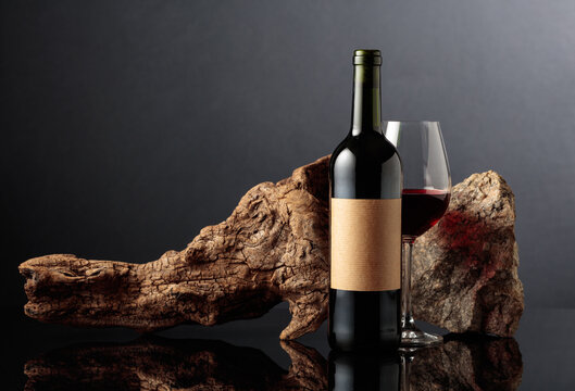 Red wine with old driftwood and a piece of granite rock on a black reflective background.