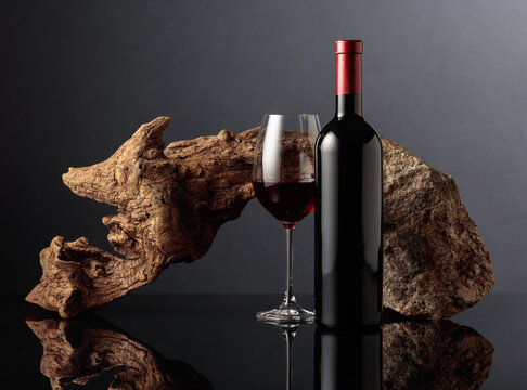 Glass and bottle of red wine with old wooden snag and a piece of granite rock.