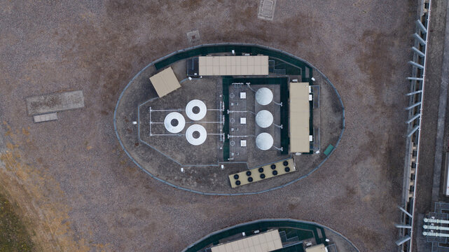 Aerial view of an industrial facility with circular tanks and rectangular buildings situated within a fenced compound in Faversham, England, United Kingdom.