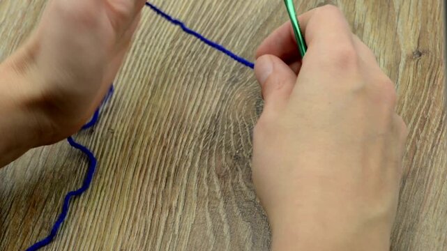 Crocheting start process close up of hands making first chain stitch with crochet hook and deep blue wool yarn in 4K Ultra HD footage.
