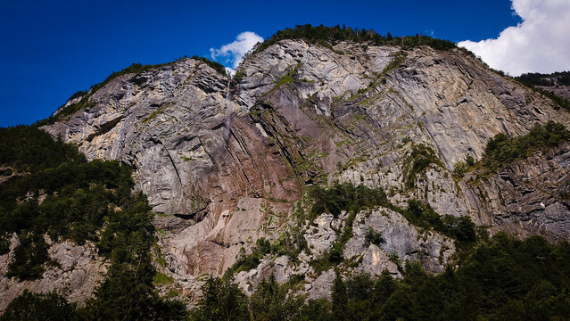 Aerial view of Cascade de l'Arpenaz falling down the steep, rugged rock face surrounded by lush forest under a blue sky in Sallanches, Auvergne-Rhone-Alpes, France.