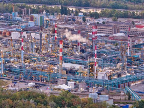 Aerial view of the industrial refinery complex with tall chimneys, intricate piping networks, and storage tanks surrounded by lush greenery in Bantzenheim, Grand Est, France.