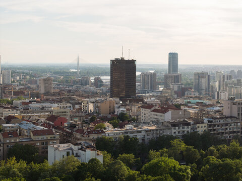 Aerial view of the Belgrade cityscape featuring modern and historic buildings, the Sava river, and the Ada Bridge under a soft sky in Belgrade, City of Belgrade, Serbia.