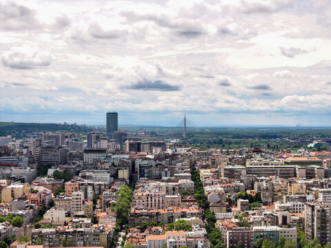 Aerial view of the dense urban cityscape of Belgrade with historic buildings, rooftops, and the distant Ada Bridge under a cloudy sky in Belgrade, City of Belgrade, Serbia.