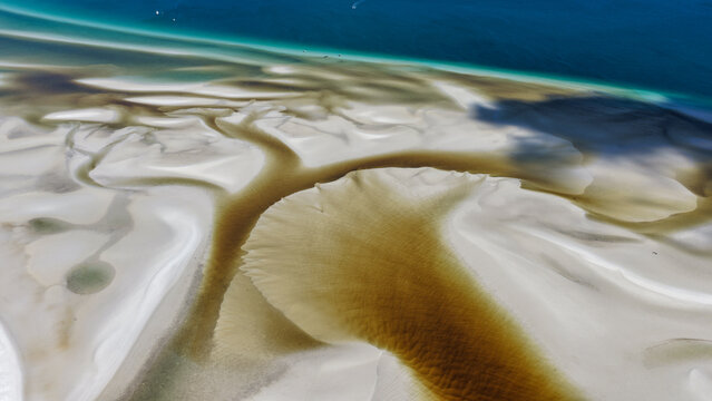Aerial view of Wathumba Creek featuring intricate patterns of white sandbars and dark tidal channels flowing into the turquoise ocean in K'gari, Queensland, Australia.