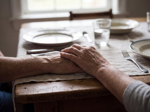 Elderly couple holding hands across wooden dining table at home