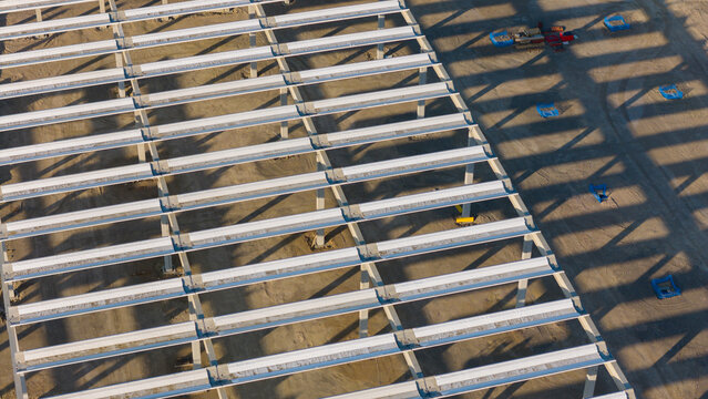 Aerial view of the construction site of a logistics park featuring concrete structural beams and long shadows cast on the dirt ground in Fiorenzuola d'Arda, Emilia-Romagna, Italy.
