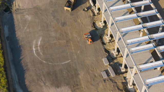 Aerial view of construction site with concrete frame structure and heavy machinery including a road roller at a logistics park in Fiorenzuola d'Arda, Emilia-Romagna, Italy.