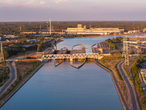 Aerial view of the canal lock system with industrial infrastructure, a bridge, and a wind turbine in Genk, Flanders, Belgium.