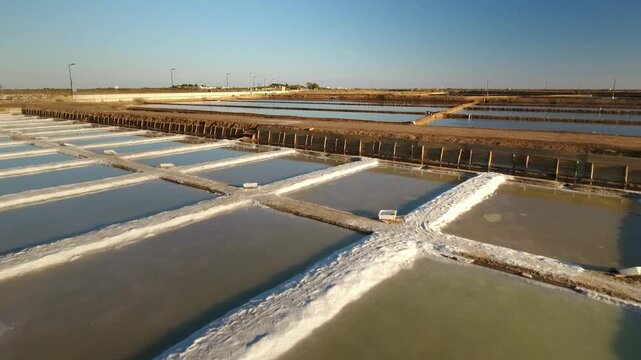 Drone perspective flying low over traditional salt evaporation ponds in tavira, portugal, revealing the geometric patterns of the salterns during the salt extraction and harvesting process