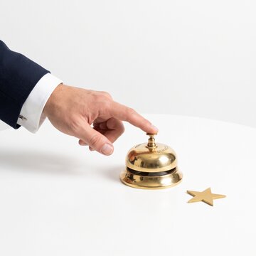 Business hand in shirt and suit blazer pressing brass hotel bell with gold star on white background