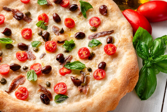 Pizza italiana con alici, pomodorini, mozzarella, olive, capperi e basilico 