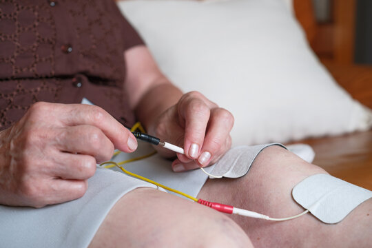 Elderly woman connecting the wires of the electrostimulation patches to treat knee pain