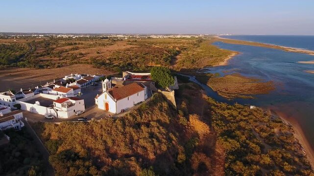 Dramatic aerial footage revealing the historic village of cacela velha, featuring its traditional church and fort overlooking the ria formosa natural park coastline in the algarve region