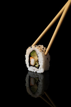 Chopsticks holding california sushi roll with reflection