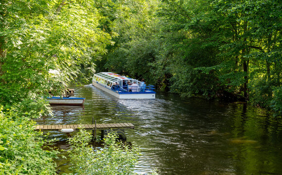 Excursion boat with tourists cruising along a canal surrounded by lush vegetation in Friedrichstadt. Water, lush vegetation and a leisurely boat trip combine tourism and recreation