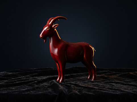 glossy statuette of red goat on black velvet fabric minimalist design of animal figurine concise object