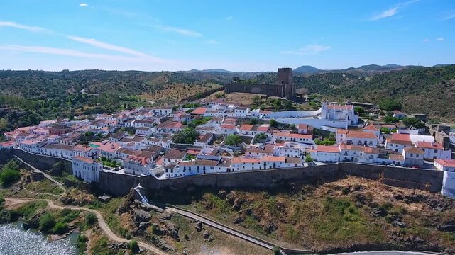 Stunning aerial footage showcasing the historic town of mertola with its whitewashed houses, ancient castle, and church overlooking the scenic guadiana river in the alentejo region of portugal