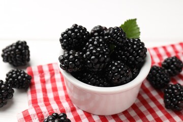 Ripe blackberries in bowl with leaf and towel on white wooden table, closeup © New Africa