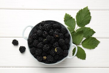 Ripe blackberries in bowl with leaves on white wooden table, flat lay © New Africa