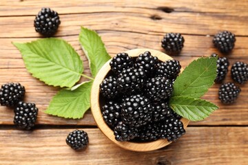 Ripe blackberries in bowl with leaves on wooden table, flat lay © New Africa