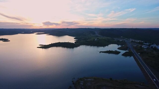 Dramatic aerial view of the odeleite dam and reservoir at sunset, with the calm water reflecting the colorful sky, showcasing the beautiful landscape of castro marim in the algarve region, portugal