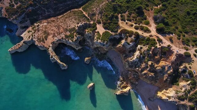 Dramatic aerial view of praia da mesquita, algarve, rugged limestone cliffs and natural arches framing turquoise atlantic waters washing onto a secluded golden sand cove