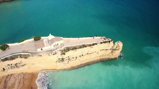Spectacular aerial view flying over chapel of nossa senhora da rocha perched on a cliff promontory above turquoise atlantic waters on the algarve coast of portugal